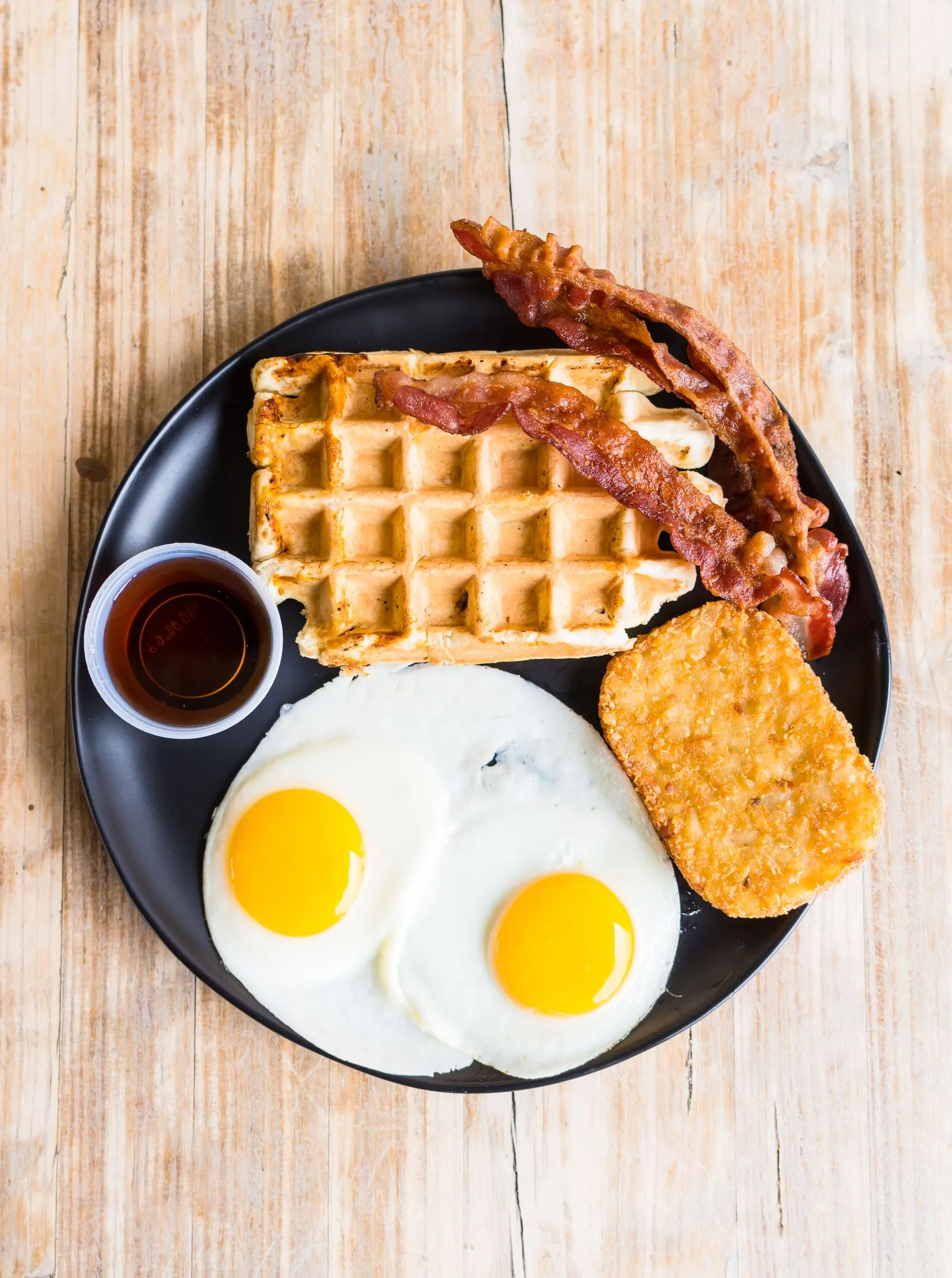 Representative breakfast platter with waffles, fried eggs, bacon, and a hash brown.