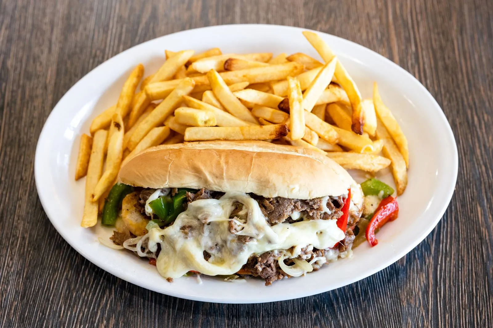 A loaded cheesesteak sub with fries.